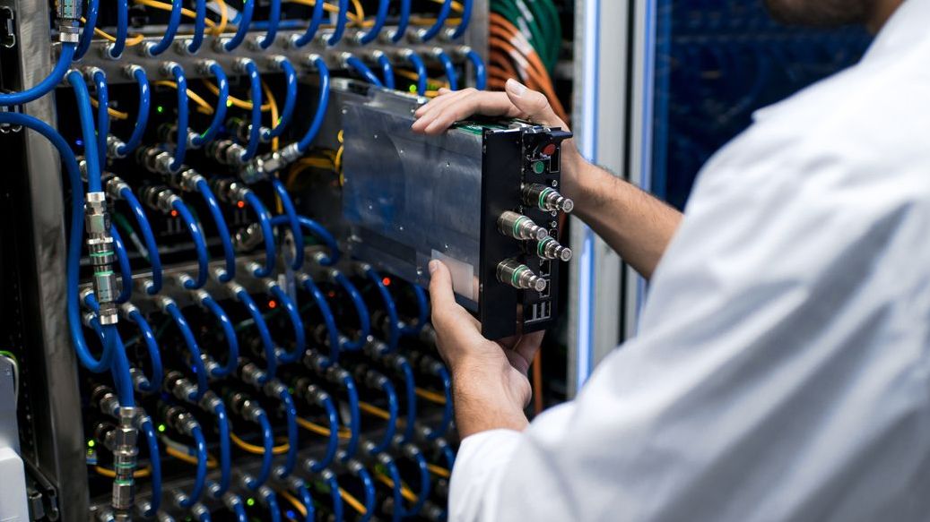 Data center commissioning: A person is installing or servicing equipment in a server room with organized blue and yellow cables in the background. They are focused on their task.