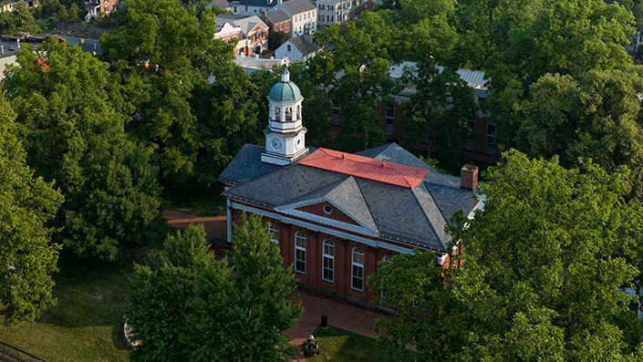 Data Center Northern Virginia: Aerial view of a classic brick building with a clock tower surrounded by lush green trees. Residential houses and streets in the background.