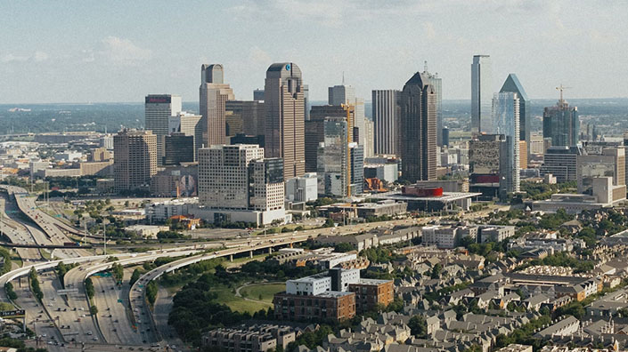 DFW data center: Aerial view of a cityscape with skyscrapers, highway intersections, and scattered buildings under a hazy sky, depicting a bustling urban environment.