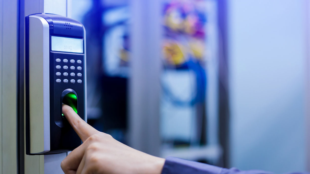 Data center physical security: A person is using a biometric fingerprint scanner for secure access, with a blurred office environment in the background. Digital and physical security concept.