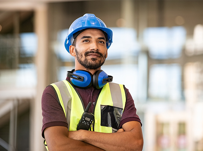A construction worker standing with his arms crossed and looking beyond