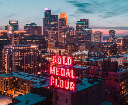 Aerial view of Minneapolis focusing on a red fluorescent sign on the top of a building that says “Gold Medal Flour”