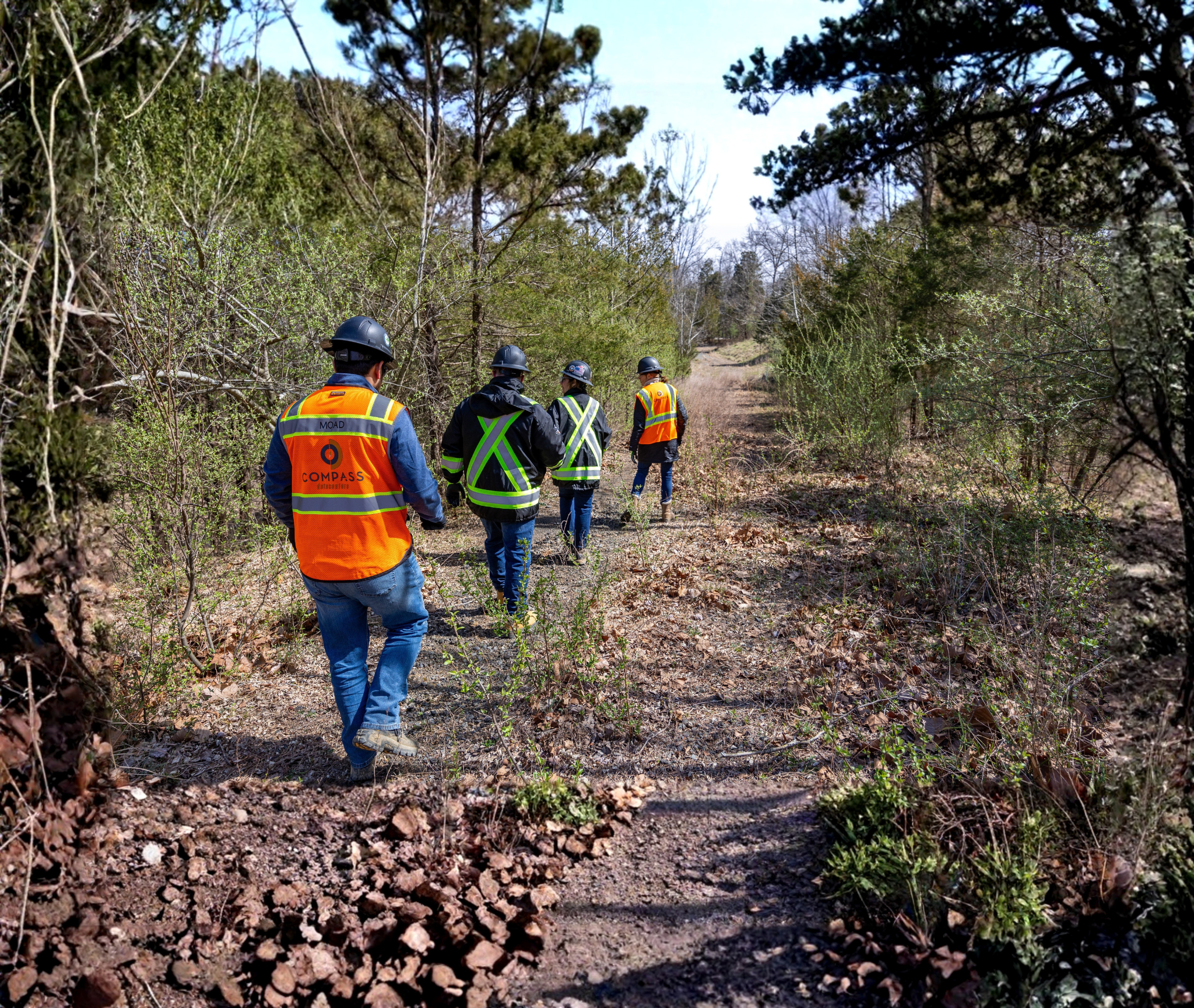 Team members wearing safety gear walking along an outdoor site path during a field assessment.