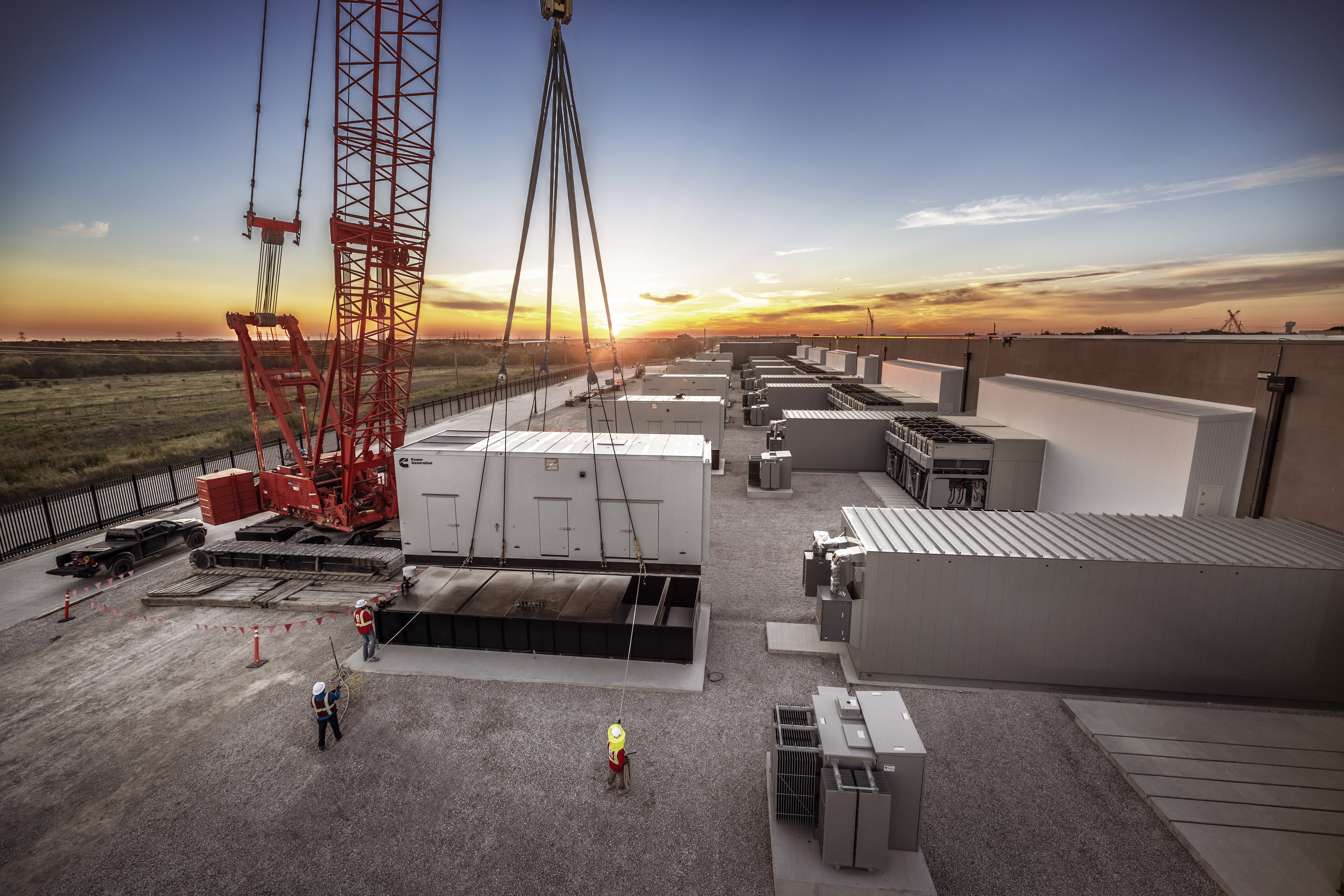 Large generator being lifted into place by a crane at a data center construction site.