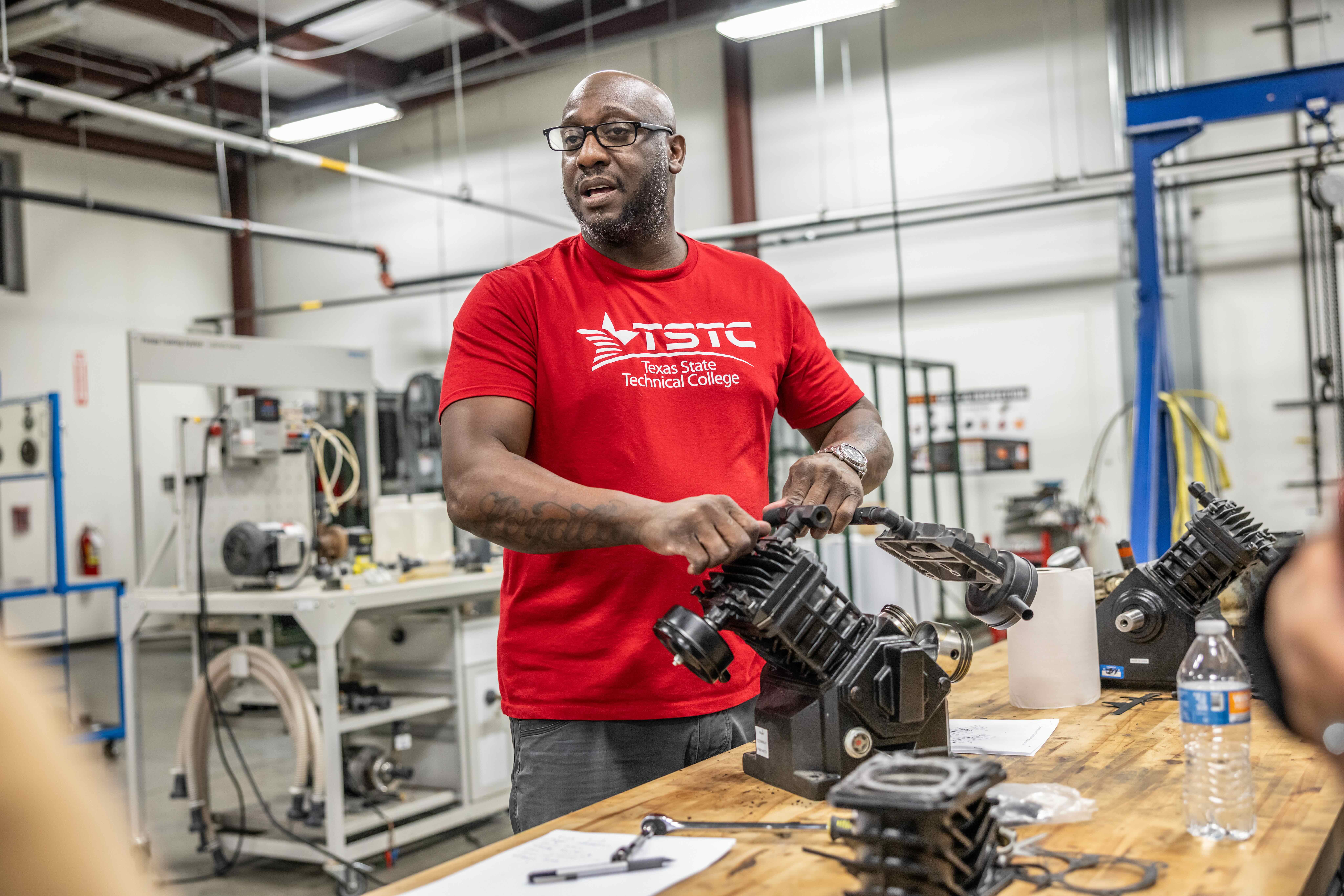 Technical instructor guiding hands-on equipment training in a classroom workshop.