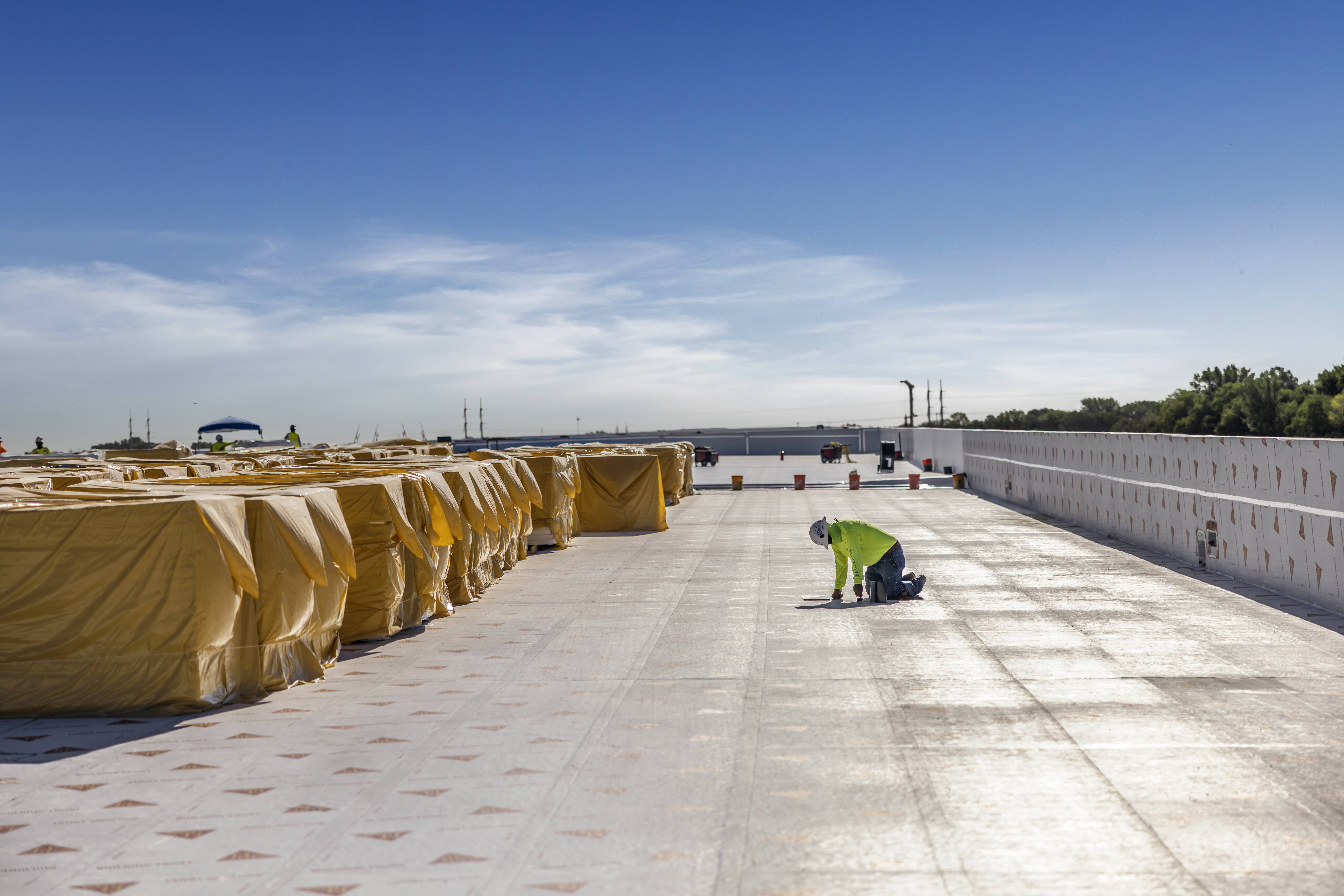Construction worker installing roofing materials on a large building under construction.